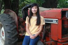 Prize winner Alysa Meng sitting in front of a red tractor and smiling.