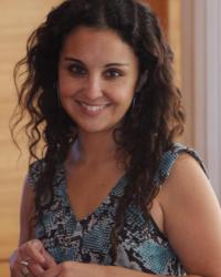 Carolina Alzamora in a blue dress, facing the camera and smiling.