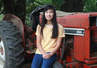 Prize winner Alysa Meng sitting in front of a red tractor and smiling.